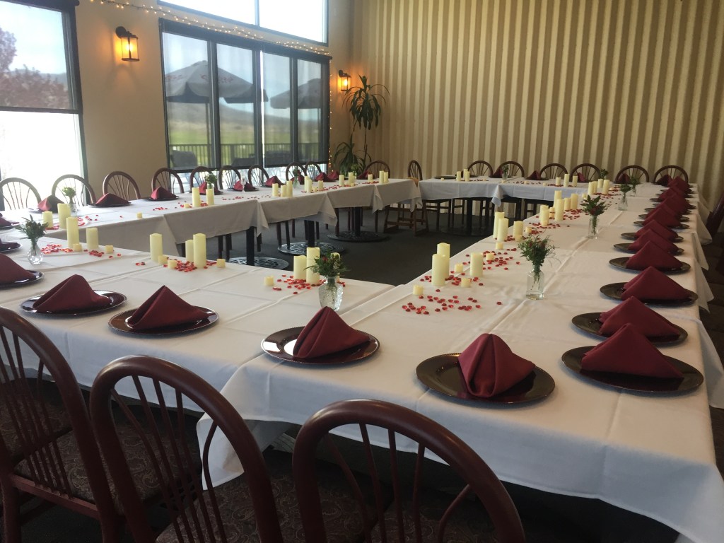 A conference room setup with red handkerchiefs on black plates. Candles and flower petals dot the table. 