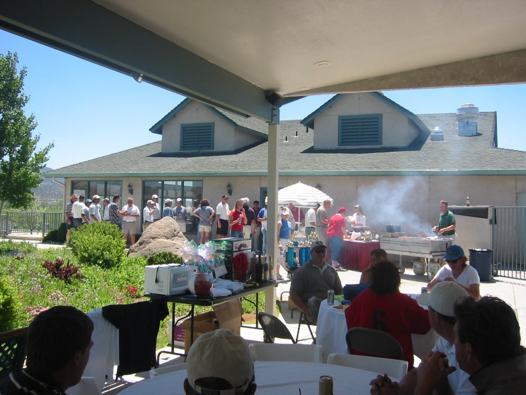 Golfers enjoying a day at the clubhouse. Golfers are lining up to  grab food cooked from a grill.